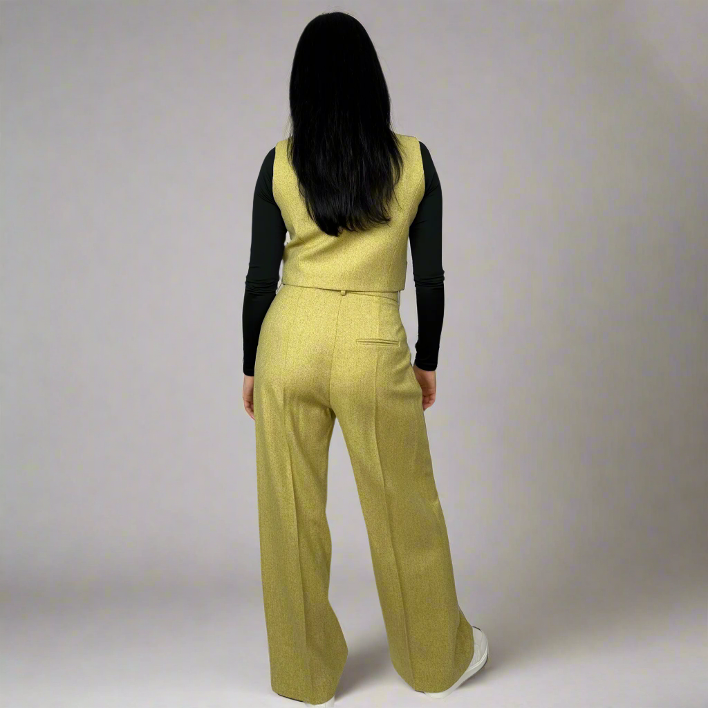 Back view of a woman modeling the Camilla mustard waistcoat, highlighting the sleek design and fit that accentuates a timeless style.