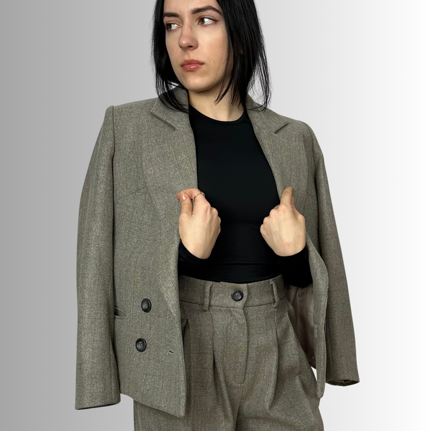 Woman adjusting Sartorial Flair Zeo double-breasted wool blazer in heather gray, sustainable fashion, paired with black top and matching tailored trousers.