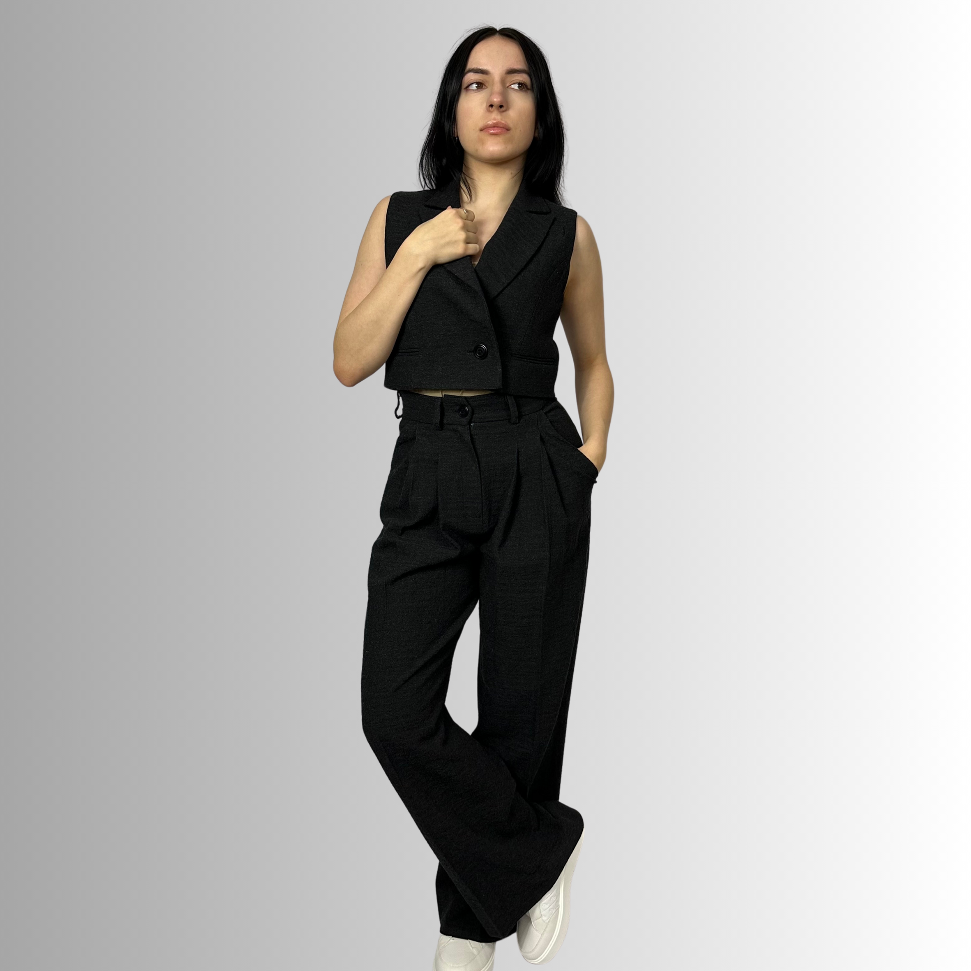 Full body view of a woman dressed in Zara black wool trousers and a matching waistcoat, presenting a sophisticated urban look with a confident stance and hand on hip.