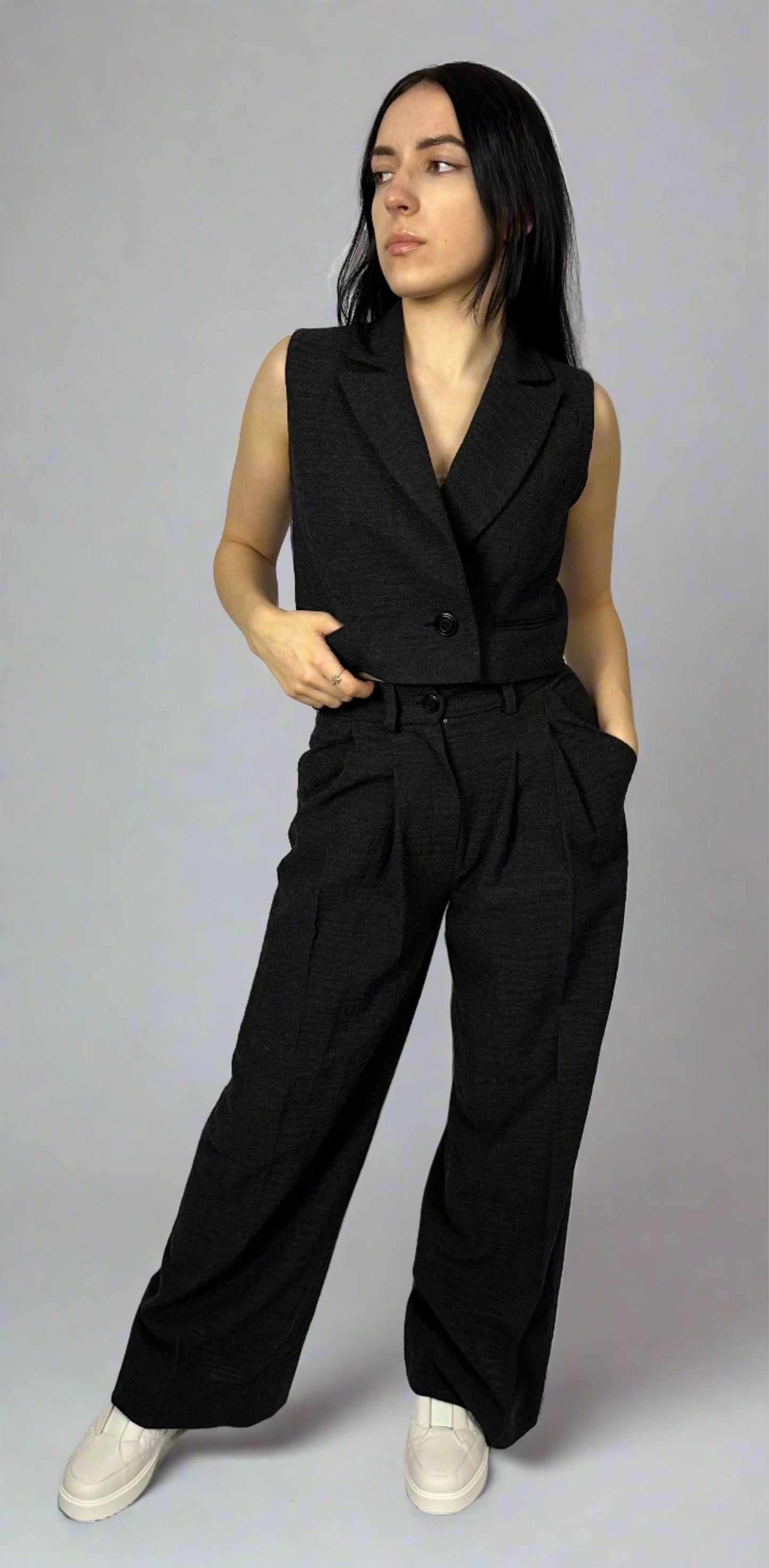 Model wearing Sartorial Flair’s black waistcoat paired with wide-leg trousers, showcasing a sophisticated and modern look. The waistcoat features a sleek, tailored fit, and the trousers offer a high waist with a pleated front, enhancing the ensemble’s elegance and professional appeal. Perfect for office wear or a stylish evening out.