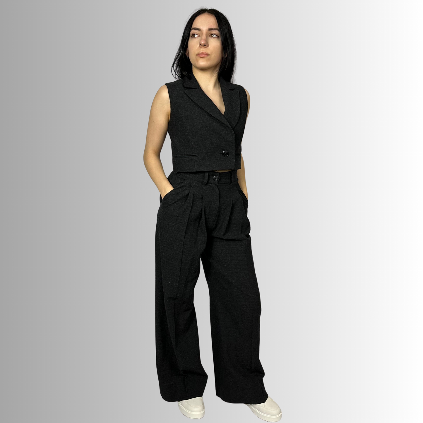 Profile view of a woman modeling Zara black trousers and waistcoat, emphasizing the sleek lines and structured fit, paired with a fitted long sleeve top.