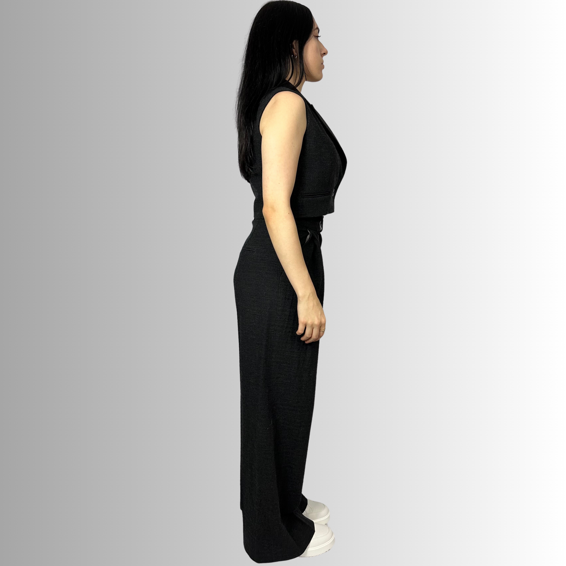 Side view of a woman wearing Zara wide-leg wool trousers and a matching waistcoat in charcoal black, with arms resting by her sides, styled with a fitted black top.